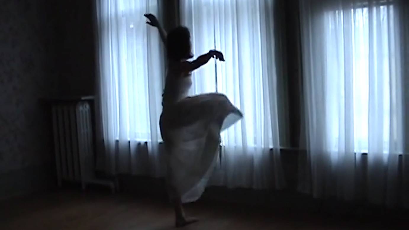 Cast in shadow, Belinda Mcguire lifts a leg while dancing against a filmy white curtain